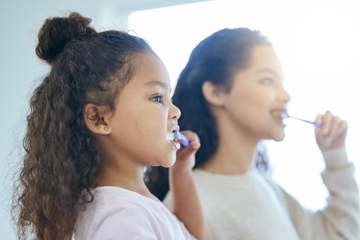 Child and mother brushing teeth together looking in the mirror