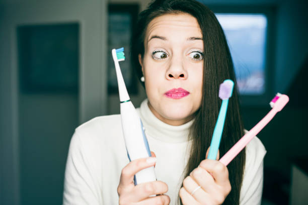 Woman looking at three different types of toothbrushes with indecision.