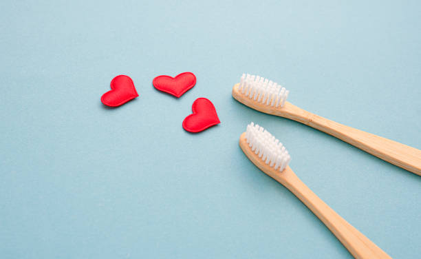 Two bamboo toothbrushes close-up with small red hearts on a blue background.