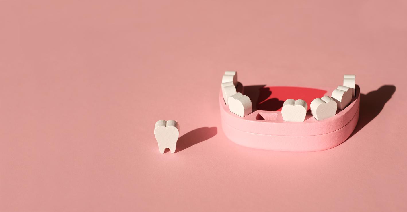 Wooden tooth set with a missing tooth on pink background.