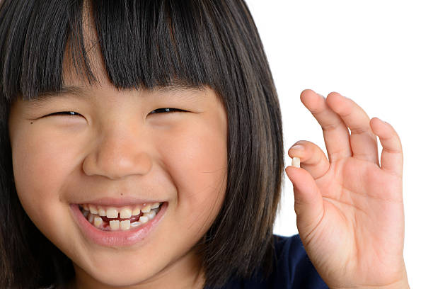 A smiling child, with gaps in their smile, holds up a shed baby tooth